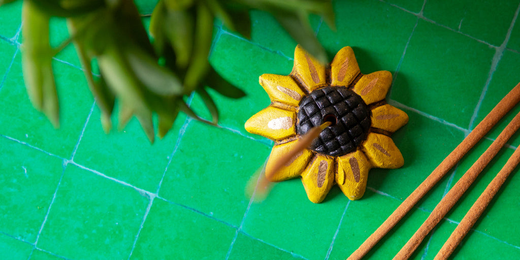 A sunflower incense holder on a green tiled background.